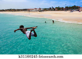 Teenage Cape verdean boy jumping on the turquoise  water of Santa Maria beach in Sal Cape Verde - Cabo Verde
