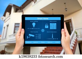 Female hands hold a tablet computer with system smart house on a screen on the background of the house