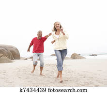 Senior Couple On Holiday Running Along Winter Beach