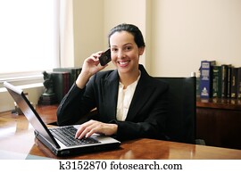 female lawyer at office talking on phone and using laptop