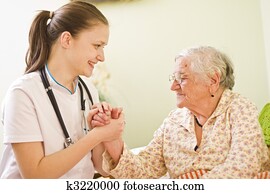 A young doctor / nurse visiting an elderly sick woman socialising - talking - with her, holding her hands.
