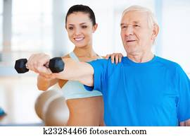 You are doing well! Cheerful female physical therapist helping senior man with fitness in health club 