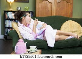 Young woman lying on sofa at home eating a sweet treat