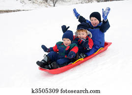 Three young boys sledding downhill together Three young boys sledding downhill together
