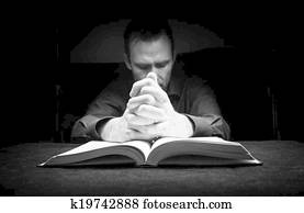 Man praying to God with his hands resting on a bible.