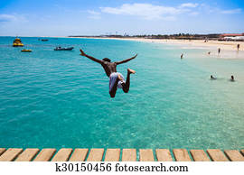 Teenage Cape verdean boy jumping on the turquoise  water of Santa Maria beach in Sal Cape Verde - Cabo Verde