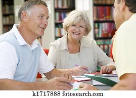 Three people in library writing in notebooks (selective focus)