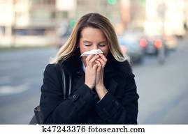 Woman with a seasonal winter cold blowing her nose Woman with a seasonal winter cold blowing her nose