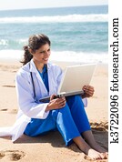 pretty nurse using laptop on beach