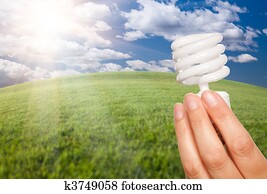 Female Hand with Energy Saving Light Bulb Over Field