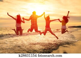 group of happy young people jumping on the beach
