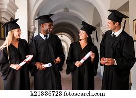 Talking about bright future. Four college graduates in graduation gowns walking along university corridor and talking