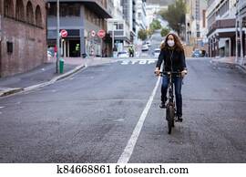 Caucasian woman wearing a protective mask and earphones, and biking in the streets Caucasian woman wearing a protective mask and earphones, and biking in the streets