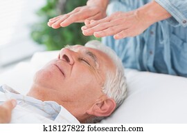 Therapist performing Reiki over senior man Therapist performing Reiki over senior man