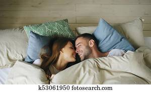 Top view of couple having fun in bed lying under blanket looking into camera and kissing at home