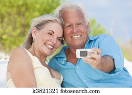 Happy Senior Couple Taking Photographs On Cell Phone At Beach