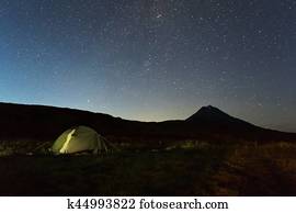 Tourist tent against night sky and Vilyuchinsky stratovolcano. Brookvalley Spokoyny at the foot of outer north-eastern slope of caldera volcano Gorely.