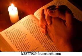 Bible by candle light with hands folded in prayer Bible by candle light with hands folded in prayer