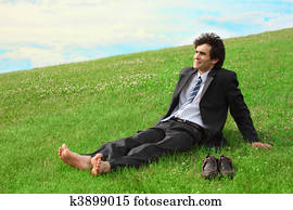 Businessman sitting on the meadow barefoot