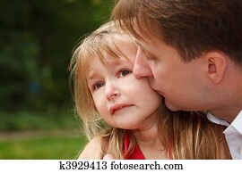 Sad little girl cries in park. Father calms her kissing on cheek.  Close up.