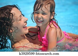 Smiling beautiful woman and little girl bathes in pool