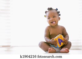 Baby sitting indoors with block smiling