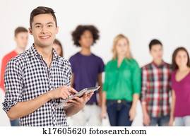 Join a digital age. Cheerful young man holding digital tablet while his friends standing on background