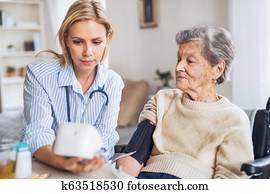 A health visitor measuring a blood pressure of a senior woman at home.