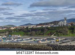 View of colorful quay and port of village Rabo de Peixe with boats, church and houses in Sao Miguel, the largest of the Azores Islands, Portugal. Sunny cloudy day