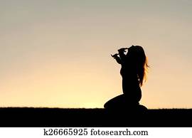 Silhouette of Woman Kneeling in Prayer and Surrender Silhouette of Woman Kneeling in Prayer and Surrender