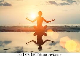Young woman silhouette in yoga lotus position on the sea beach, in bright colors.