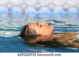 Woman face relaxing floating on water of a pool or spa