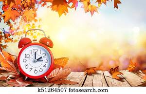 Daylight Savings Time Concept - Clock And Leaves On Wooden Table Daylight Savings Time Concept - Clock And Leaves On Wooden Table