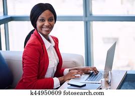 Black businesswoman smiling at the camera while seated on sofa