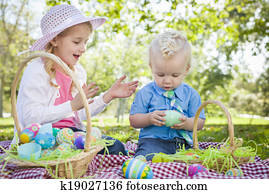 Cute Young Brother and Sister Enjoying Their Easter Eggs Outside in the Park Together.