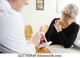 Doctor Explaining Shoulder Rotator Cuff Model To Senior Woman