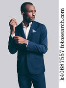 Perfect style. Handsome young African man in full suit adjusting his  sleeve and looking away while standing against grey background