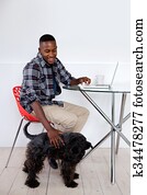 Young african man sitting at home with his pet dog and laptop