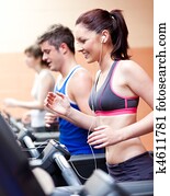 Beautiful female athlete standing on a running machine listening to the music in a fitness centre Beautiful female athlete standing on a running machine listening to the music in a fitness centre