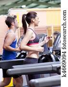 Pretty woman with earphones using a treadmill with her boyfriend in a fitness centre