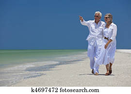 Happy Senior Couple Walking Pointing To Sea on Tropical Beach