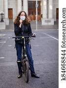 Caucasian woman wearing a protective mask on her bike, wearing earphones in the streets Caucasian woman wearing a protective mask on her bike, wearing earphones in the streets