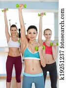 Weight training. Three beautiful young women in sports clothing exercising with dumbbells and smiling at camera