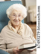 Senior Woman Relaxing In Chair At Home Reading Book