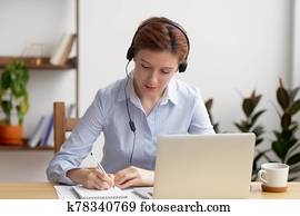 fokussiert, frau, in, kopfhörer, laptop benutzend, schreiben notizen