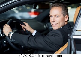 I love this car. Side view of cheerful senior man in formalwear sitting in car and looking over shoulder