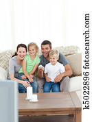 Happy family laughing while watching television sitting on the sofa at home Happy family laughing while watching television sitting on the sofa at home