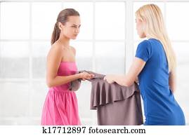 This dress is mine! Two angry young women holding one dress together and looking at each other