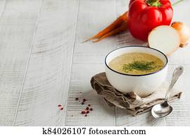 Homemade broth in a white bowl on a napkin with dill and fresh vegetables on a wooden background. Copy space. Homemade broth in a white bowl on a napkin with dill and fresh vegetables on a wooden background. Copy space.