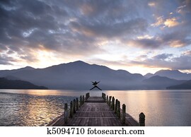 Successful businessman jumping on the pier and watching sunrise and mountain